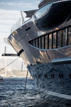 The mesmerizing reflection of the water on the glossy side of a huge yacht anchored, chrome details, chains and ropes to the muring descend into the water. High quality photo