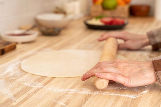 Faceless woman roll out dough with rolling pin on kitchen table at home, apartment, flour, scales, bowls, digital tablet with recipes on table. Homemade food