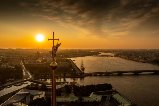 The golden angel on the cross of the Peter and Paul Fortress at sunrise, reflection of the orange sky on the water, drawbridges Troitsky and Liteiny . High quality photo