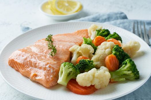 Steam salmon and vegetables, Paleo, keto, fodmap, dash diet. Mediterranean diet with fish. Healthy concept, white plate on gray table, gluten free, lectine free, side view, close up