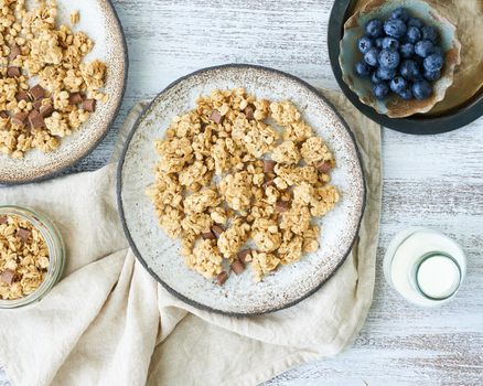 Yogurt with chocolate granola, bilberry. Breakfast, healthy diet food with oat flakes, nuts, banana, rustic wooden table, top view