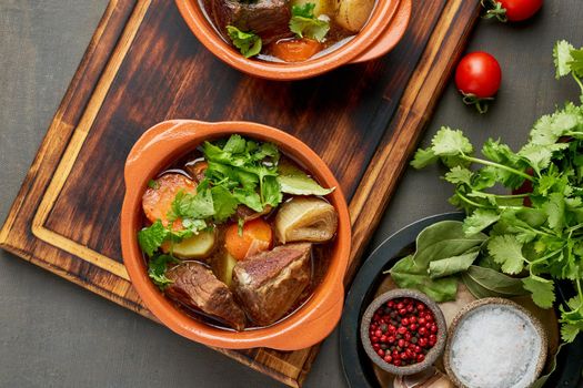 Goulash with large pieces of beef and vegetables. Burgundy meat. Slow stewing, cooking in two pot or cast-iron pan. Dark backdrop. Top view, banner