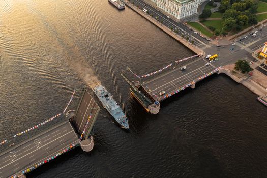 Aerial landscape of warship pass under a raised Palace drawbridge, top view, black color of water, the Neva River before the holiday of the Russian Navy at early morning. High quality 4k footage