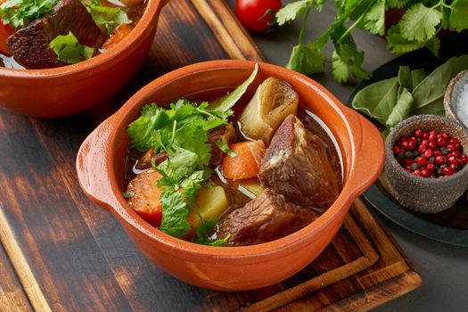 Goulash with large pieces of beef and vegetables. Burgundy meat. Slow stewing, cooking in two pot or cast-iron pan. Dark backdrop. Side view