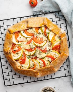 Homemade savory galette with vegetables, wholegrain pie with tomatoes, zucchini, blue cheese Gorgonzola. Rustic crust crostata on dark linen textile tablecloth. Top view, vertical