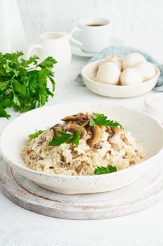 Risotto with mushrooms in plate. Rice porridge with mushrooms and parsley. White table, spoons, mushrooms. Hot dish, italian cuisine, side view, vertical