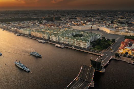 Aerial landscape with warships in the Neva River before the holiday of the Russian Navy at early morning, warships pass under a raised drawbridge, the latest cruisers among landmarks, Palace bridge. High quality photo