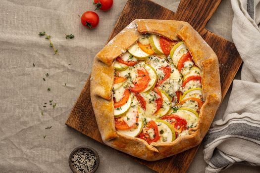 Homemade savory galette with vegetables, wheat pie with tomatoes, zucchini, blue cheese Gorgonzola. Rustic crust crostata on dark linen textile tablecloth. Top view, copy space