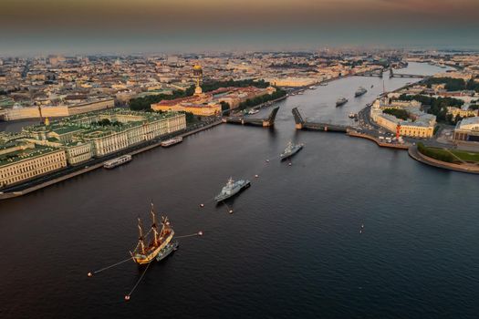 Aerial landscape with warships in the Neva River before the holiday of the Russian Navy at early morning, warships pass under a raised drawbridge, the latest cruisers among landmarks, Palace bridge. High quality photo