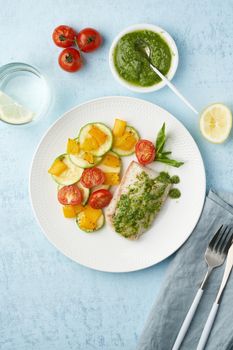 Keto dinner with white fish. Oven baked fillet of cod, pike perch with vegetables and pesto sauce. Healthy diet food, ketogenic paleo diet, Mediterranean cuisine. Blue background. Top view, vertical