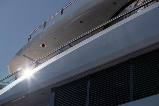 The top deck of a huge yacht at sunny day, glossy board of the boat, The chrome plated handrail, megayacht is moored in port, sun reflection on glossy board. High quality photo