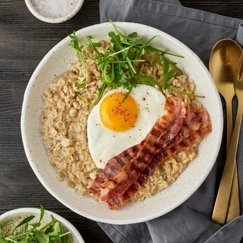Oatmeal, fried egg and fried bacon. Brutal man sport breakfast. Hearty fat high-calorie breakfast, source of energy. Balance of proteins, fats, carbohydrates. Balanced food. Macro