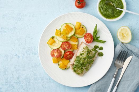 Keto dinner with white fish. Oven baked fillet of cod, pike perch with vegetables and pesto sauce. Healthy diet food, ketogenic paleo diet, Mediterranean cuisine. Blue background. Top view, copy space