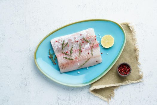 Fillet of raw white walleye fish on a blue plate on a white background. Whole piece of fresh fish with herbs and lemon. Top view