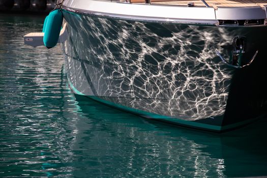 The mesmerizing reflection of the water on the glossy side of a huge yacht anchored, chrome details. High quality photo