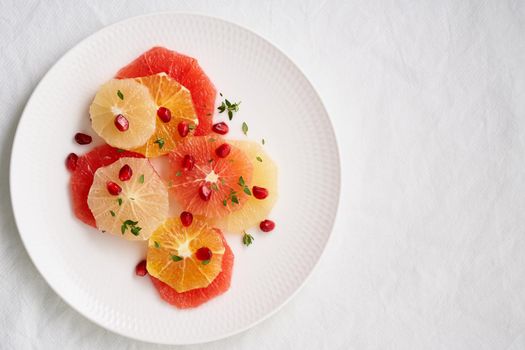 Bright mix of citrus fruits, vertical. Salad of mix sliced round slices of red and white grapefruit sprinkled with pomegranate seeds on white plate. Copy space