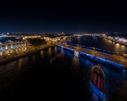 night landscape of festivities on the day of the Russian Navy, picturesque night illumination of buildings, warships and drawbridges, many people walk in the absence of automobile traffic. High quality photo
