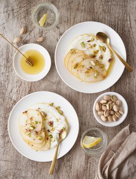 Ricotta with pears, pistachios and honey or maple syrup on two white plate on wooden table. Sweet and healthy dessert. Vertical