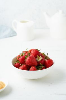 Strawberries in white bowl, on white table, morning Breakfast, summer food, light background. Vertical