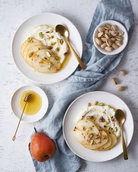 Ricotta with pears, pistachios and honey or maple syrup on two white plate on gray table. Sweet and healthy dessert. Vertical