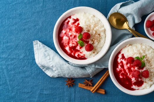 Rice pudding. French milk rice dessert with raspberries, blueberries, berries, jam. Healthy Vegan diet breakfast with coconut milk, cinnamon. Blue linen textile. Top view, copy space