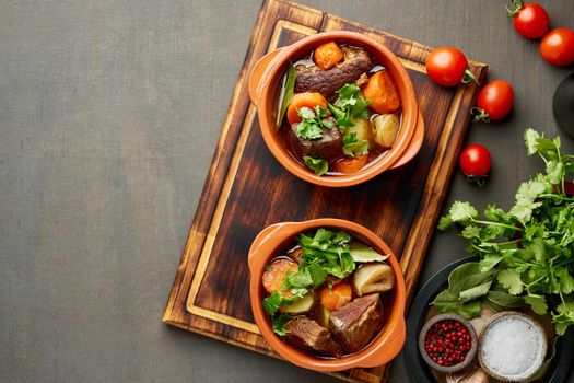 Goulash with large pieces of beef and vegetables. Burgundy meat. Slow stewing, cooking in pot or cast-iron pan. Dark brown backdrop. top view, copy space