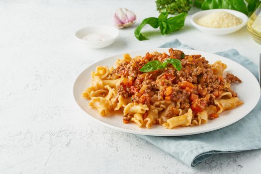 Pasta Bolognese campanelle with mincemeat and tomato sauce, parmesan cheese, basil. Italian dinner, white table. , side view, close up, copy space