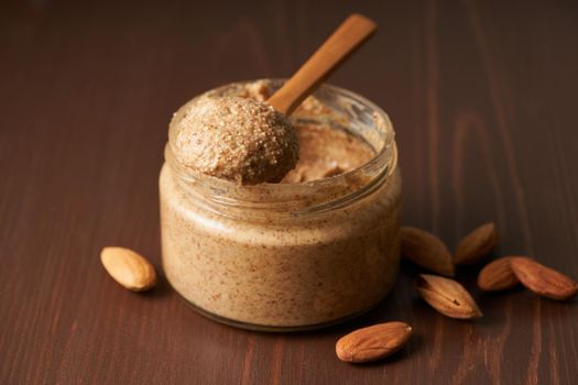almond butter, raw food paste made from grinding almonds into nut butter, crunchy and stir, dark brown wooden table, copy space, side view, close up