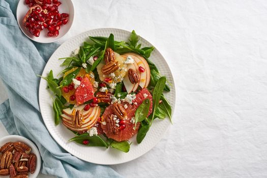 Fruits citrus salad with nuts, green lettuce leaves. Balanced food. Spinach with orange, grapefruit, apples, pecans and gorgonzola, garnished with pomegranate seeds, top view, copy space