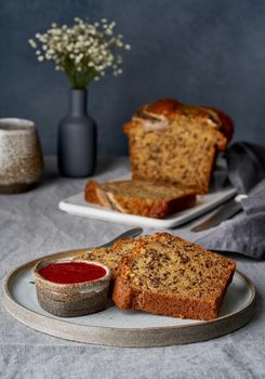 Banana bread. Cake with banana, traditional american cuisine. Slices of loaf with raspberry jam. Dark background, black table, shadows. Side view, close up.