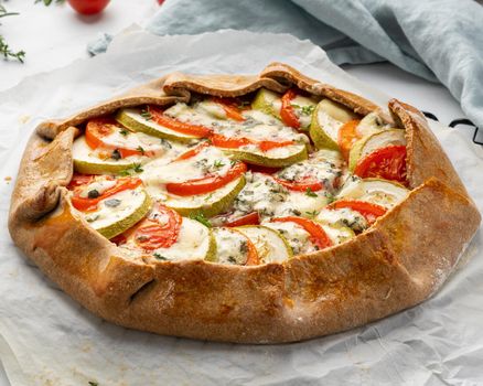 Homemade savory galette with vegetables, wholegrain pie with tomatoes, zucchini, blue cheese Gorgonzola. Rustic crust crostata on dark linen textile tablecloth. Side view