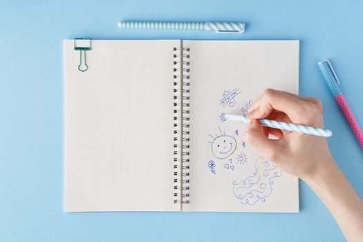 Hand draws scribble in a notebook. Blank notepad page in bullet journal on bright blue office desktop. Top view of modern table with notebook, stationery. Mock up, copy space