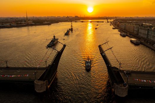 Aerial landscape with warships in the Neva River before the holiday of the Russian Navy at early morning, warships pass under a raised drawbridge, the latest cruisers among landmarks, Palace bridge. High quality photo