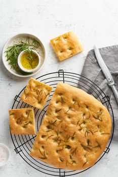 Focaccia, pizza, italian flat bread with rosemary and olive oil on grid on white rustic table, tradition italian cuisine, top view, copy space, vertical