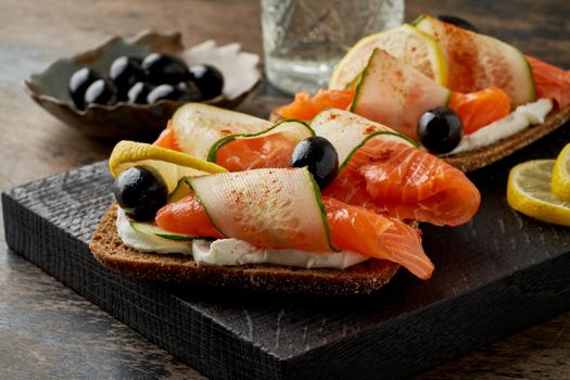 Smorrebrod - traditional Danish sandwiches. Black rye bread with salmon, cream cheese, cucumber and olives on dark brown wooden background