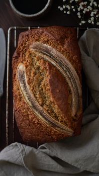 Banana bread. Cake with banana, traditional american cuisine. Whole loaf. Dark background, black table, shadows. Vertical, top view, close up.