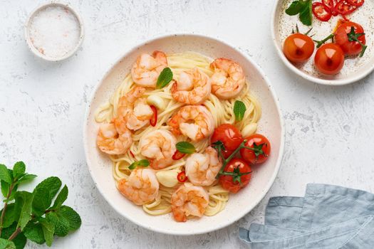 Pasta bavette with fried shrimps, bechamel sauce, mint leaf, garlic, tomatoes, chili on white plate, top view, italian cuisine.