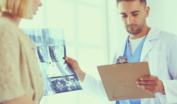 Handsome doctor is talking with young female patient and making notes while sitting in his office