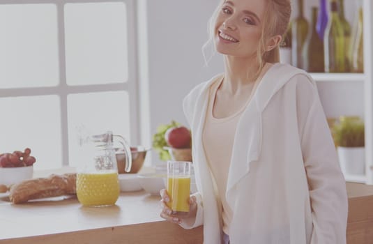 Attractive woman holding a glass of orange juice while standing in the kitchen.