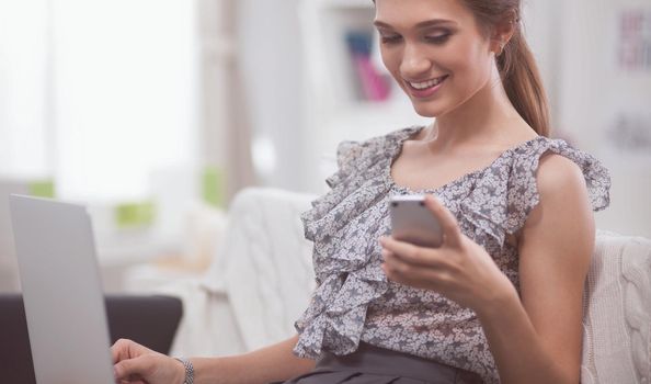 Young smilingYoung smiling beautiful woman sitting on the sofa with phone and laptop. beautiful woman sitting on the sofa with phone and laptop