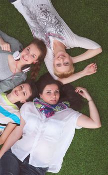 Four young women lying on green grass .