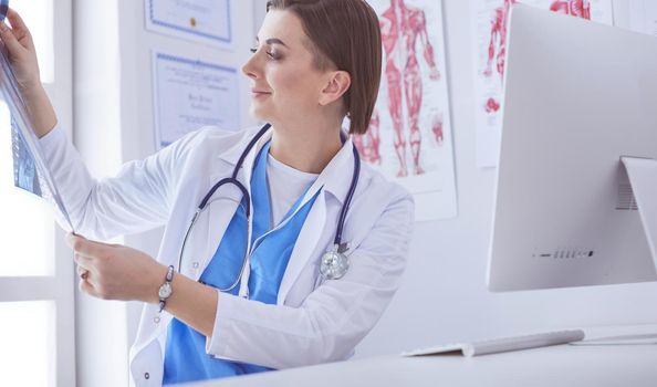 Portrait of doctor sitting in office holding xray image, working on computer.