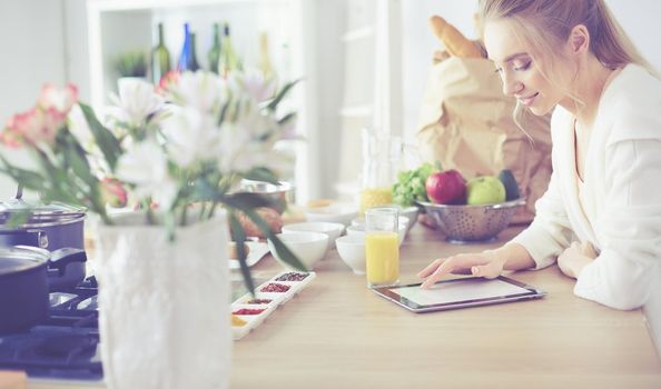 Beautiful young woman using a digital tablet in the kitchen.
