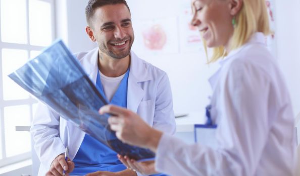 Handsome doctor is talking with young female doctor and making notes while sitting in his office