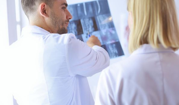 Handsome doctor is talking with young female doctor and making notes while sitting in his office