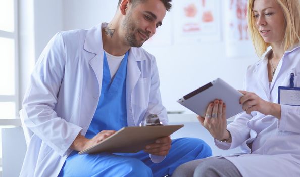 Handsome doctor is talking with young female patient and making notes while sitting in his office.