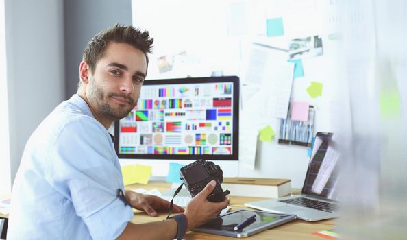 Portrait of young designer sitting at graphic studio in front of laptop and computer while working online