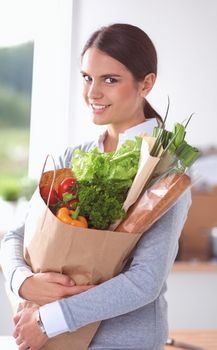 Young woman holding grocery shopping bag with vegetables .Standing in the kitchen.