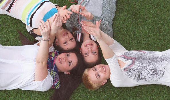 Four young women lying on green grass with hands up .