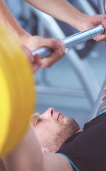 Young man lifting the barbell in the gym with instructor .